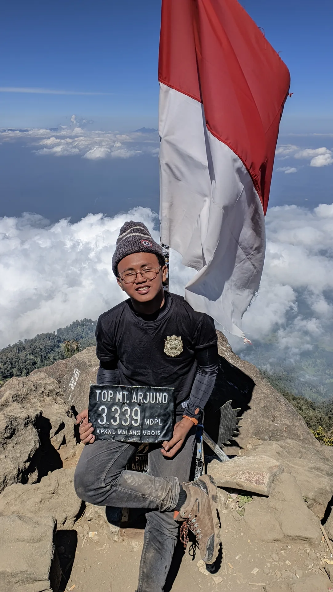 Ahmad Farrel holding a summit marker beneath the Indonesian flag on Mount Arjuna