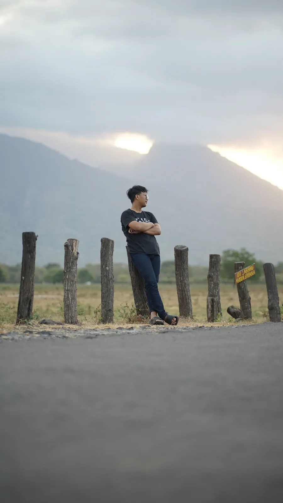 A person standing along the road beneath a cloudy mountain sky