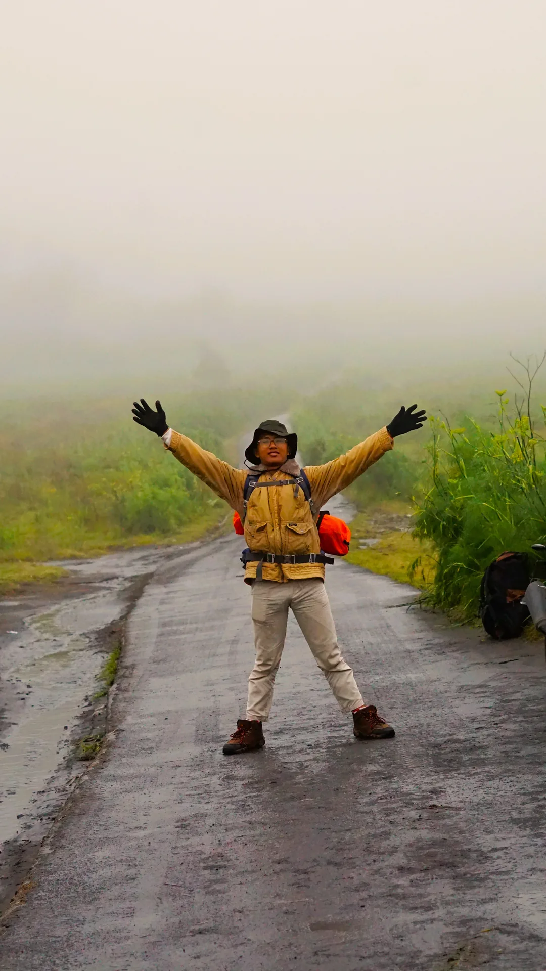 Traveller raising both arms on a wet, misty road in the Bromo highlands