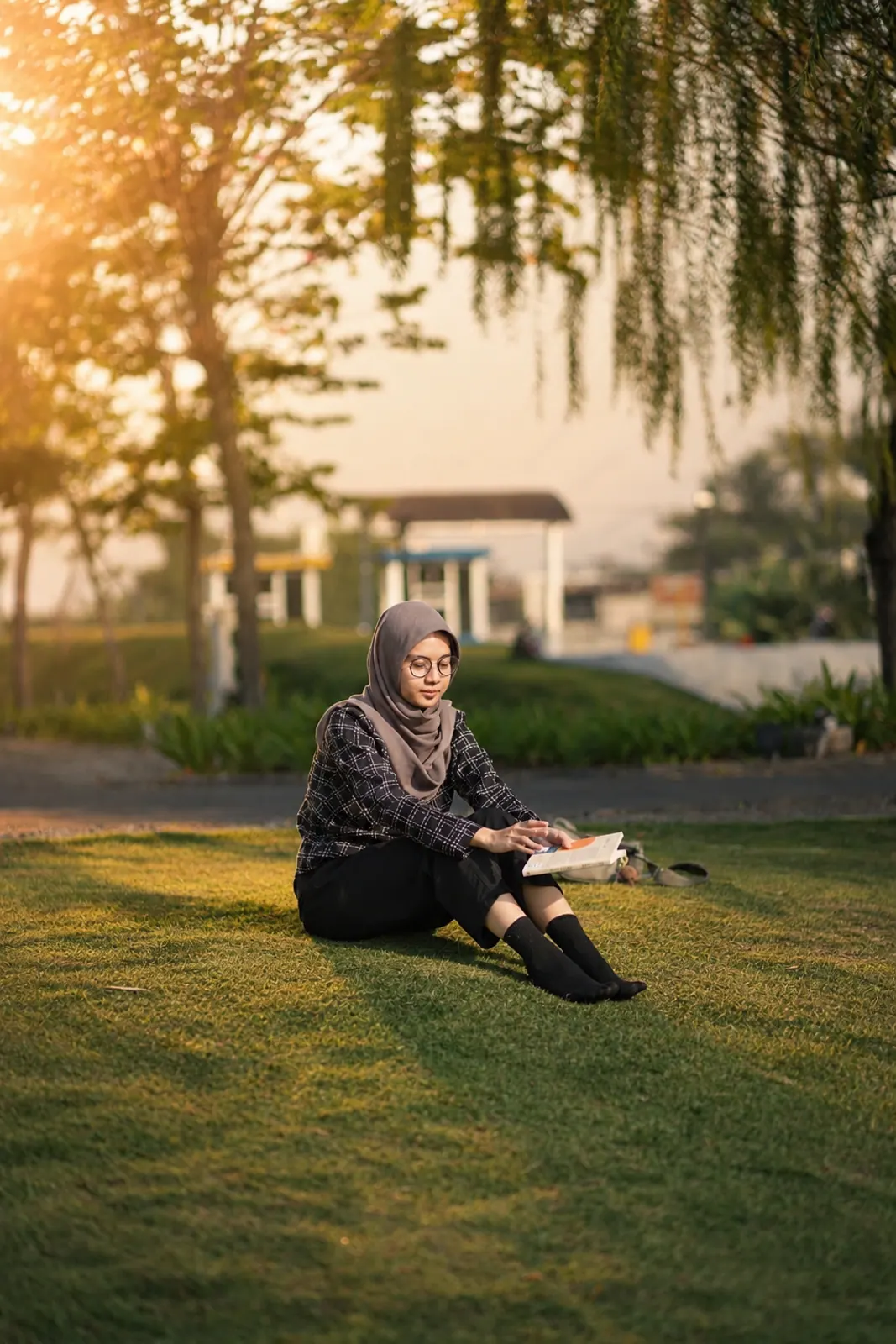A woman seated on the grass with a book at golden hour
