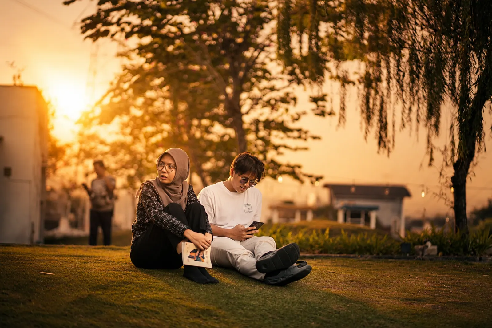 Two people seated together beneath a tree in golden light