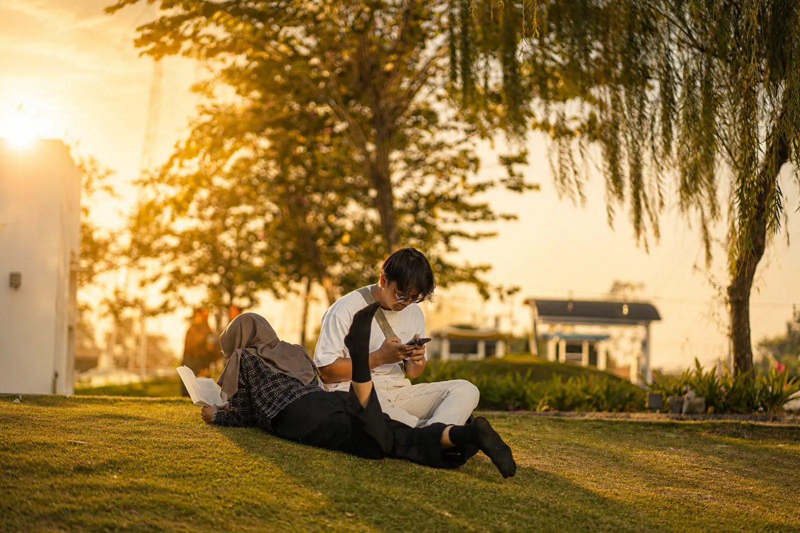 Two people reading together on the grass at sunset