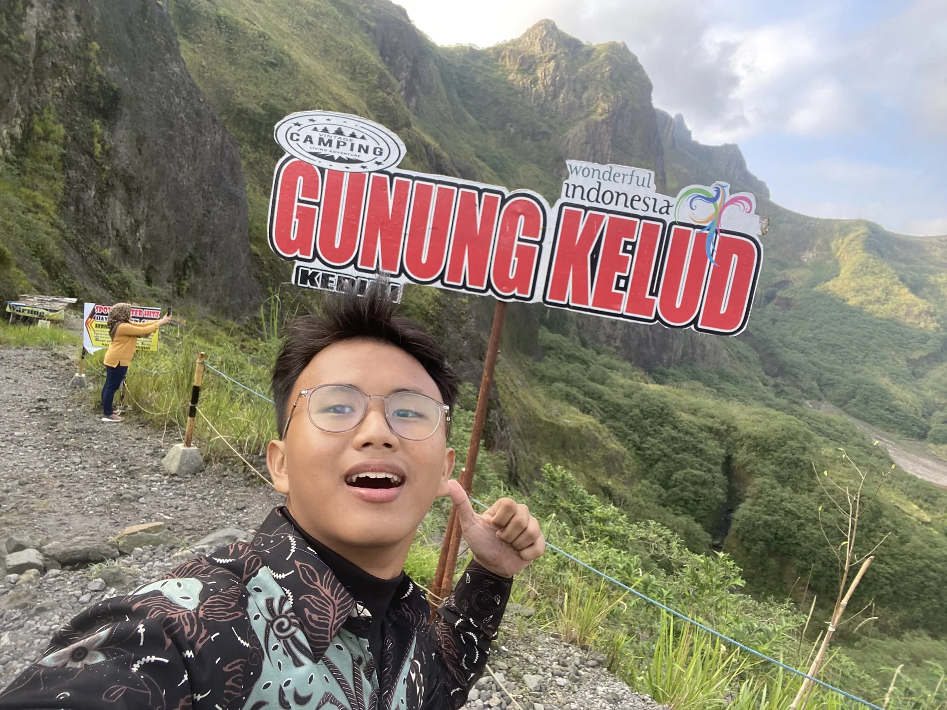 Ahmad Farrel taking a selfie beside the Gunung Kelud sign and mountain ridge