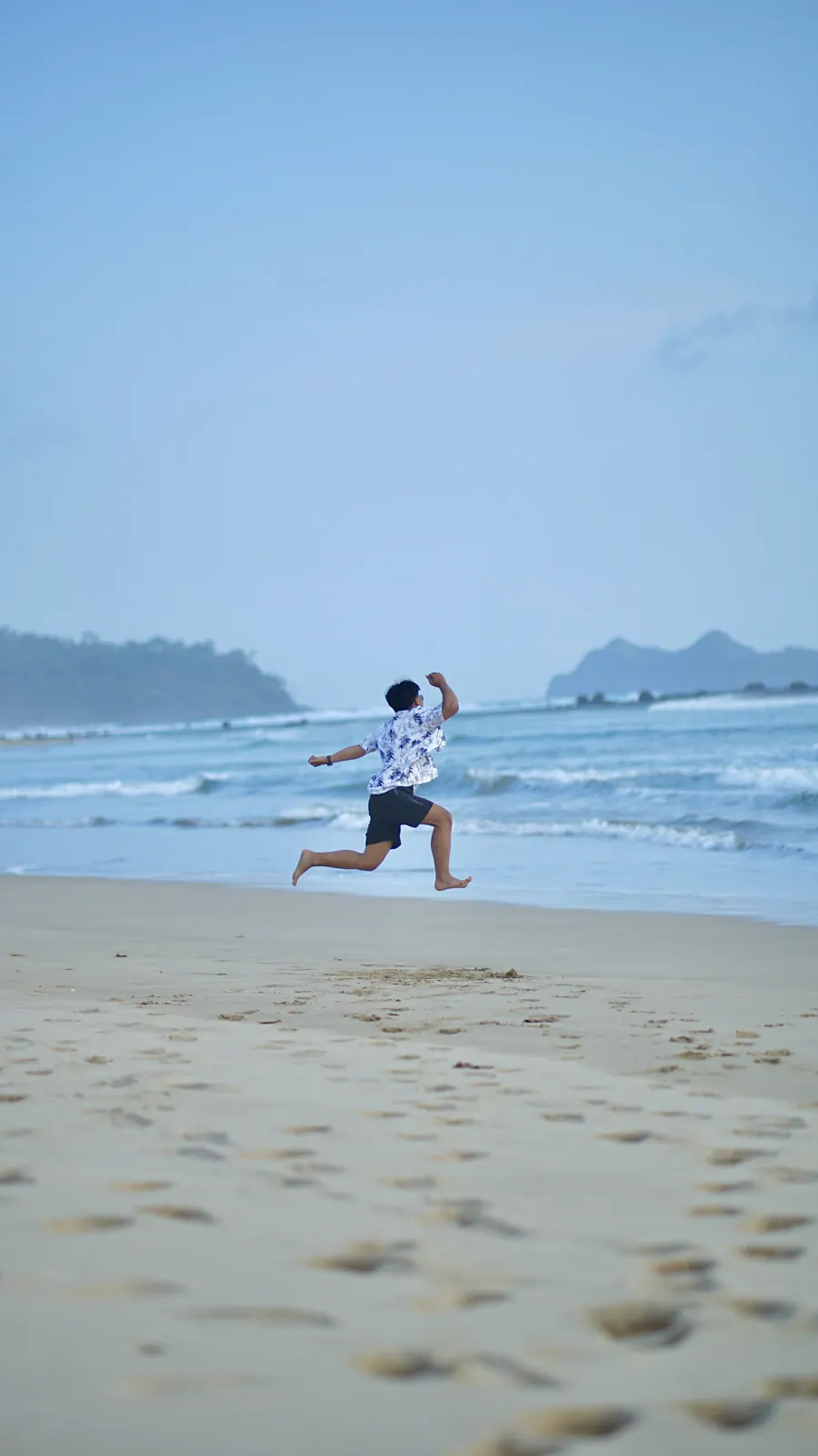 Ahmad Farrel jumping on the beach with the sea behind him